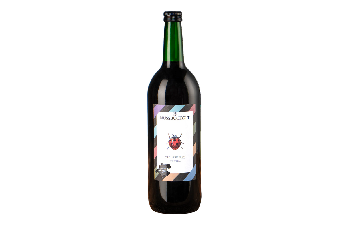 Es ist eine 1 l Traubensaftflasche dargestellt. Am Etikett befindet sich neben dem Nussböckgutlogo ein hübscher Marienkäfer, welcher uns bei der Arbeit im Weingarten stets Freude bereitet.
